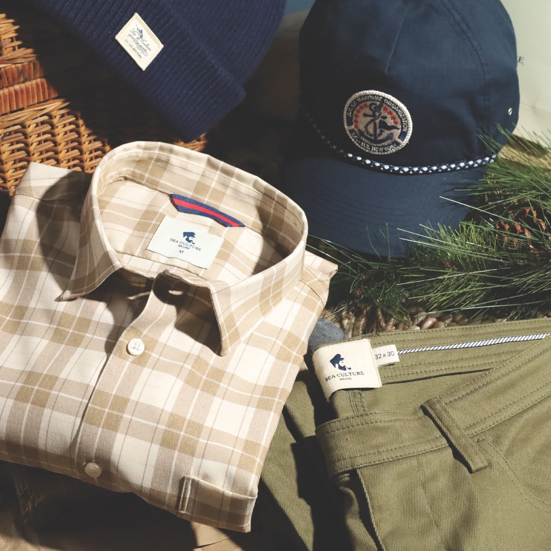 Plaid shirt, olive trousers and navy headwear arranged with pine branches